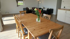 A spacious dining area with a wooden table and chairs, a vase of tulips, a painting on the wall, and a view of the outdoors through a window.
