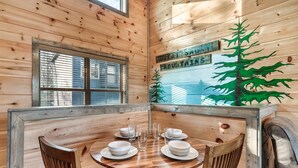 A wooden cabin interior with a dining table set for four, surrounded by wooden chairs. - Great Location/Close to Dollywood/HotTub/Arcade/Mountain View/Dog Friendly (Sevierville)