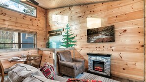 A cozy cabin interior with wooden walls, a fireplace, a dining area, and a large window. - Great Location/Close to Dollywood/HotTub/Arcade/Mountain View/Dog Friendly (Sevierville)