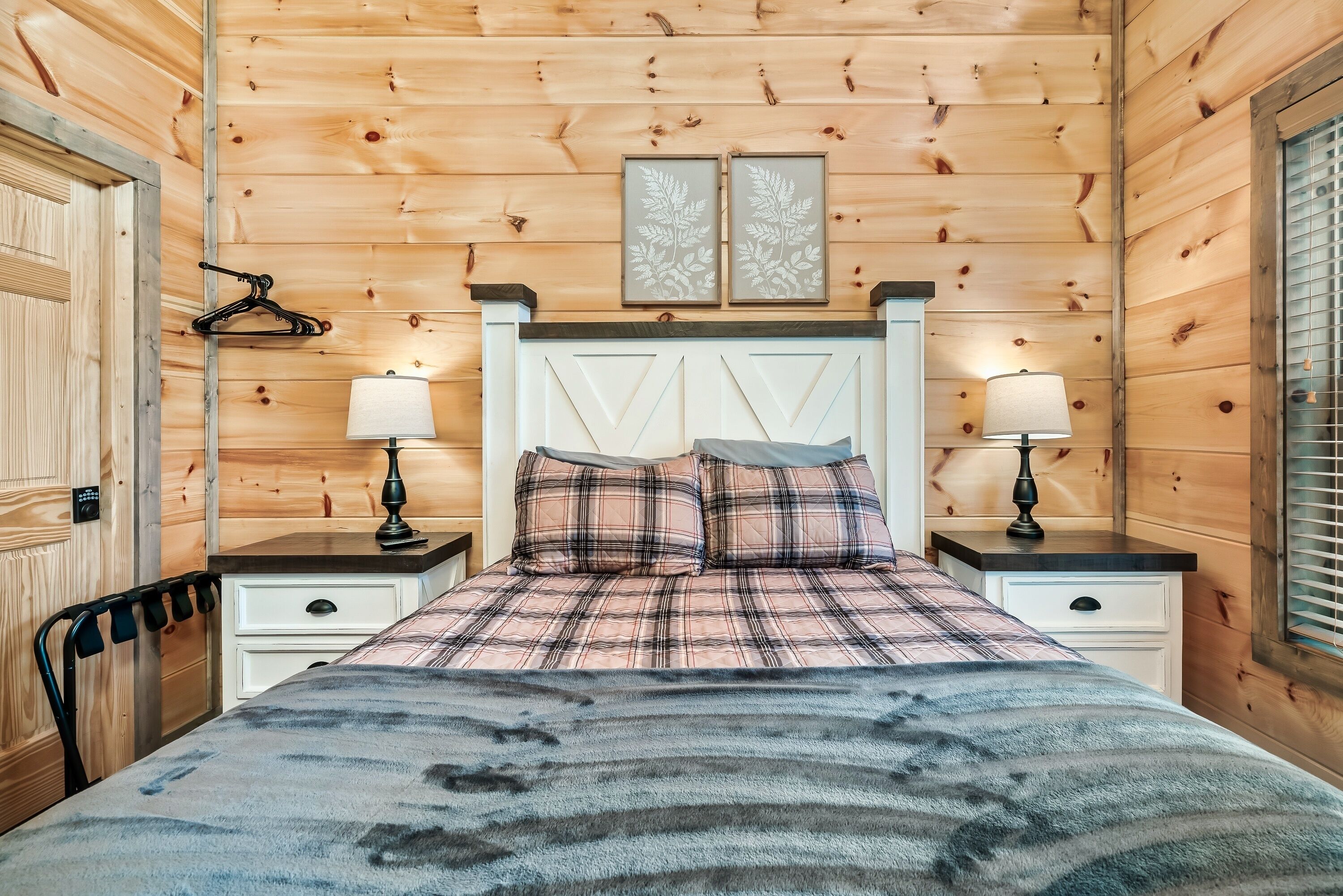 A wooden-paneled bedroom with a bed, two bedside tables, and a hanging coat rack.