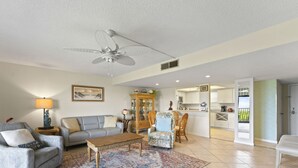 A spacious living room with a ceiling fan, a sofa, a coffee table, and a dining area with chairs. - Direct Oceanfront Condo on the Beach w/ Private Balcony, Heated Pool & Steps to Pier! (Cocoa Beach)