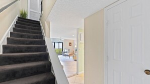 A staircase leading to a living area with a door, a plant, and a view of the outdoors. - Direct Oceanfront Condo on the Beach w/ Private Balcony, Heated Pool & Steps to Pier! (Cocoa Beach)