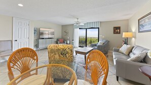 A spacious living room with a balcony, a sofa, two wicker chairs, a coffee table, and a TV. - Direct Oceanfront Condo on the Beach w/ Private Balcony, Heated Pool & Steps to Pier! (Cocoa Beach)