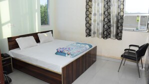 A bedroom with a wooden bed, white bedding, a patterned throw, a black chair, and a window with a curtain. - Hotel Sleep Inn    (Sonepat)