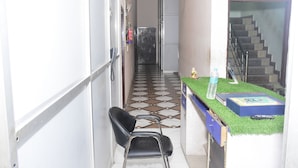 A narrow hallway with a tiled floor, a black chair, a small table with a water bottle, and a staircase in the background. - Hotel Sleep Inn    (Sonepat)