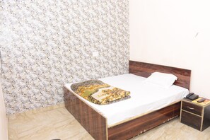 Een net opgemaakt bed met een bedsprei met dessin, een houten hoofdbord en een nachtkastje met telefoon en afstandsbediening.