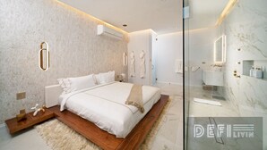 Ein modernes Schlafzimmer mit einem großen Bett, einem Nachttisch aus Holz, einem flauschigen Teppich und einer Duschkabine aus Glas.