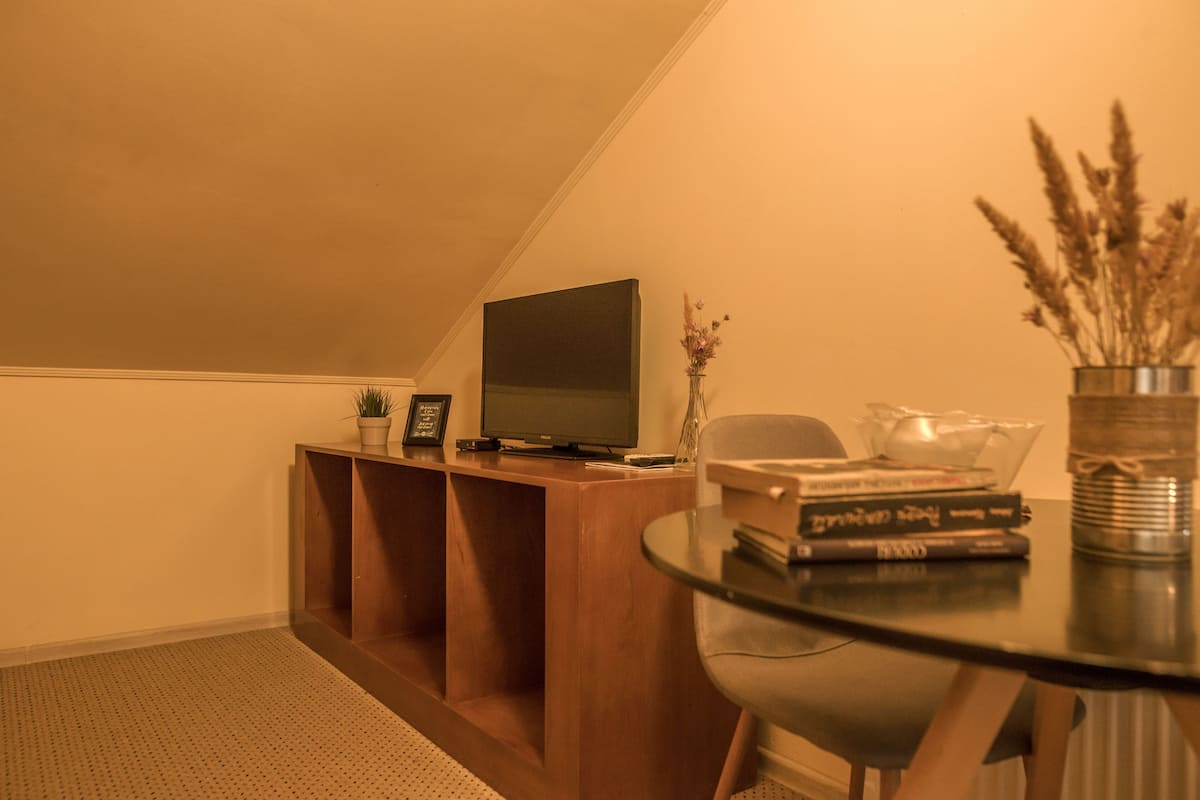 Ein gemütliches Zimmer mit einer Holzeinrichtungsanlage, einem Flachbildfernseher, einem Glastisch mit Büchern und einer Vase mit getrockneten Blumen.