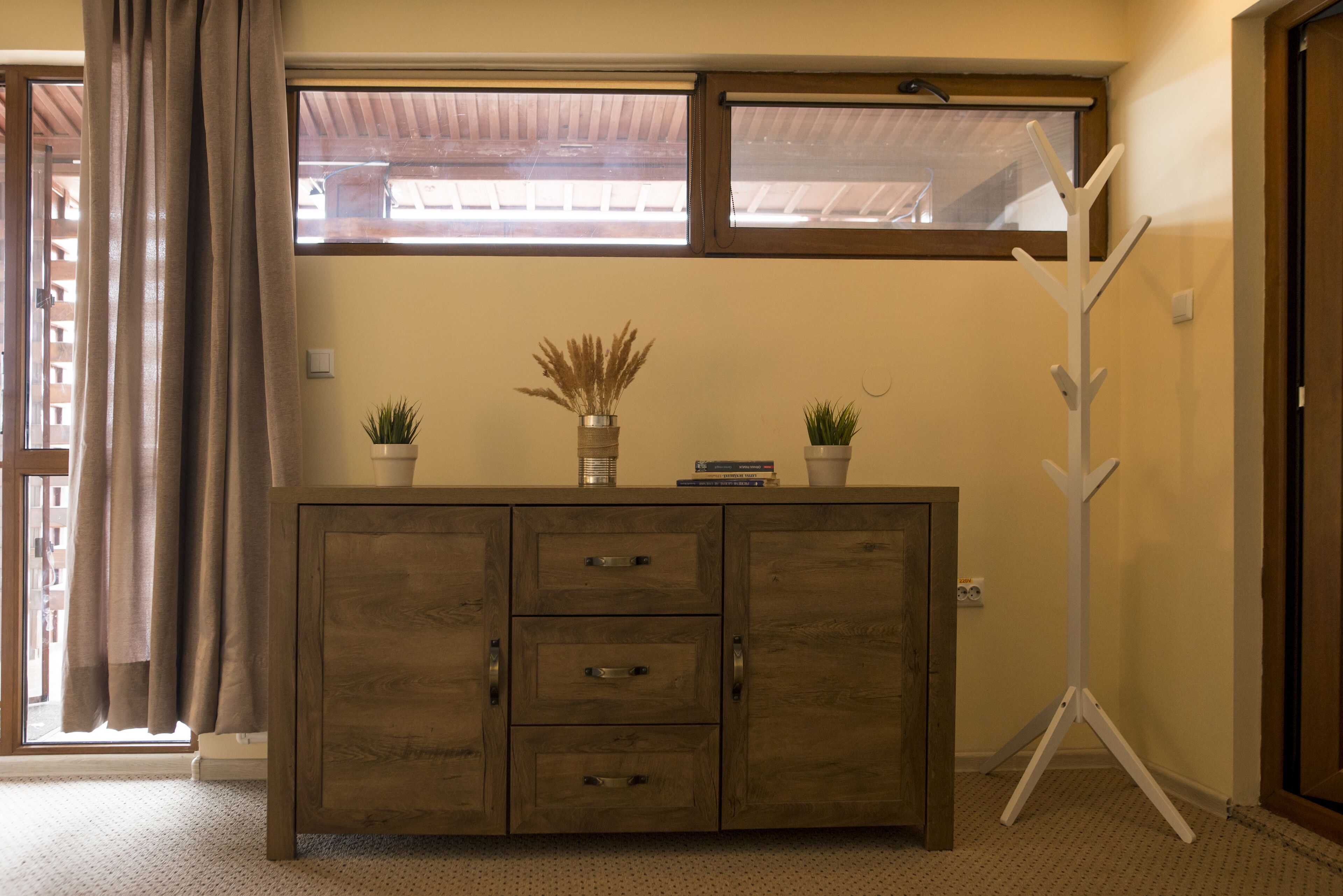 A wooden cabinet with drawers, a window above, and a coat rack to the right.
