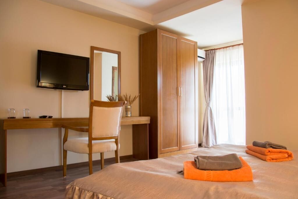 A hotel room with a bed, a desk, a chair, a television, a wardrobe, and a window with curtains.