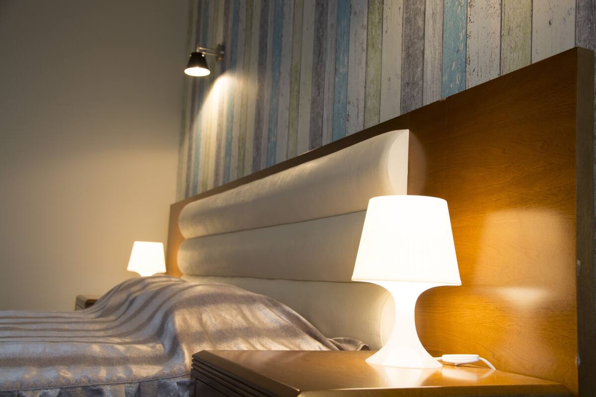 Ein ordentlich bezogenes Bett mit Kopfteil, einer Nachttischlampe und einer Wand mit Streifenmuster.