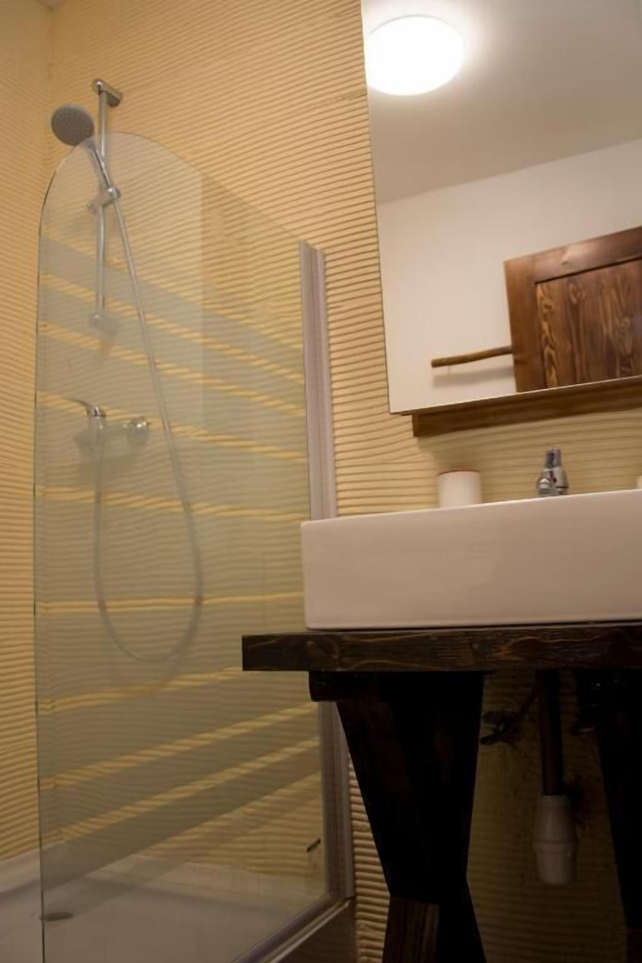 Un baño con cabina de ducha de vidrio, tocador de madera y espejo sobre el lavabo.