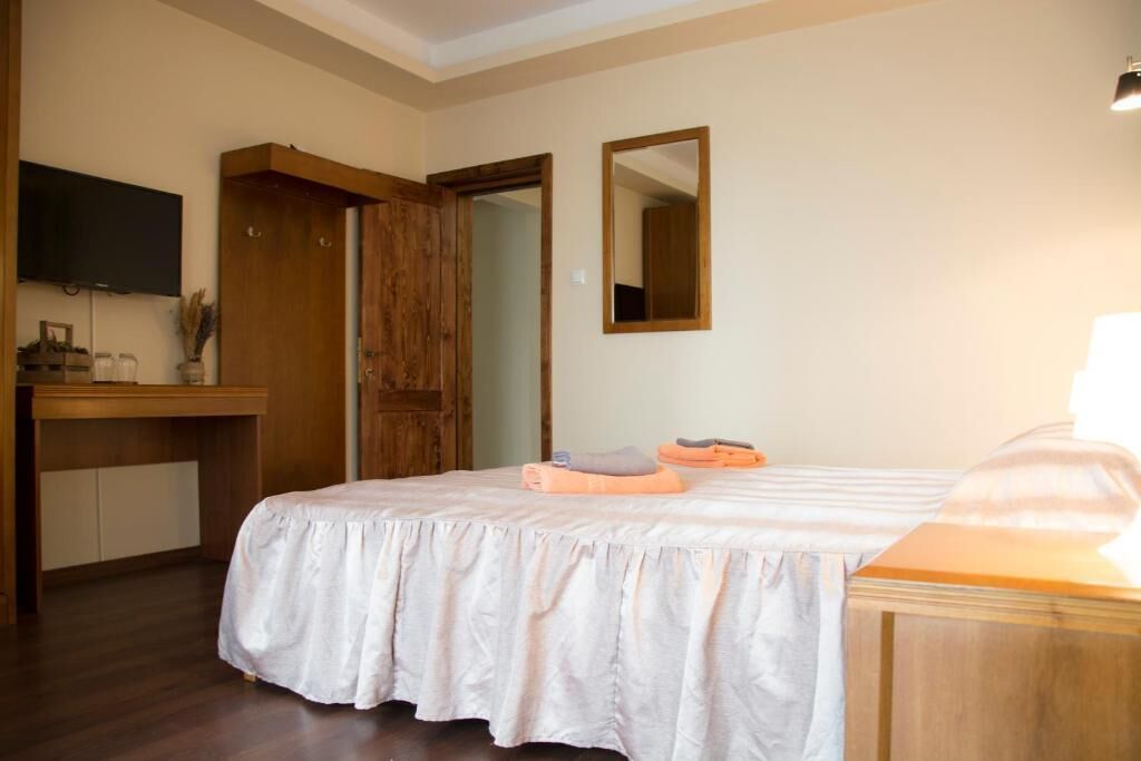 A bedroom with a bed, a wooden desk, a television, and a mirror.