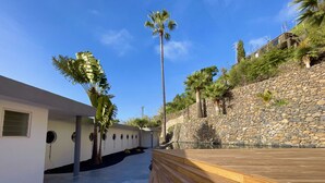 Un espacio exterior moderno con un muro de piedra, palmeras y una terraza de madera.