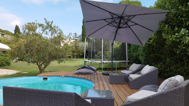 Ein Poolbereich mit Holzterrasse, Korbmöbeln und einem großen Sonnenschirm.