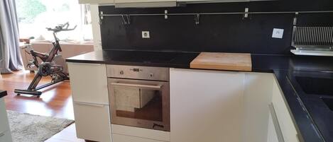 Una cocina compacta con armarios blancos, una encimera negra, un horno empotrado y una pequeña tabla de cortar de madera.