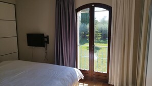 Ein Schlafzimmer mit einem Bett, einem an der Wand montierten Fernseher und einer Glastür, die auf einen Balkon führt.