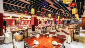 Un restaurant doté de nombreuses tables et chaises, de murs rouges et de lanternes suspendues.