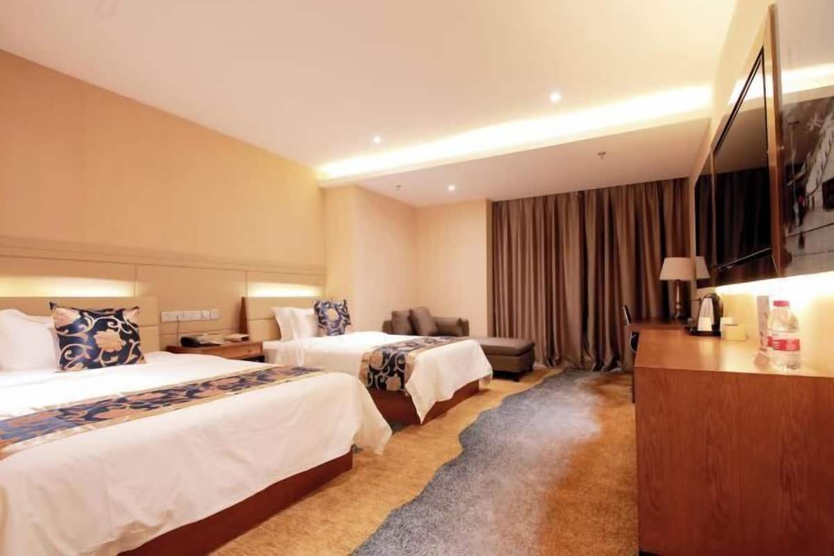 A hotel room with two beds, a desk, a television, and a large window with curtains.