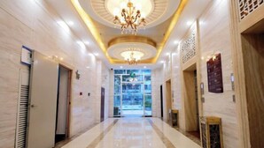 Un couloir d’hôtel avec un lustre, un sol en marbre et une porte en verre donnant sur un hall d’entrée.