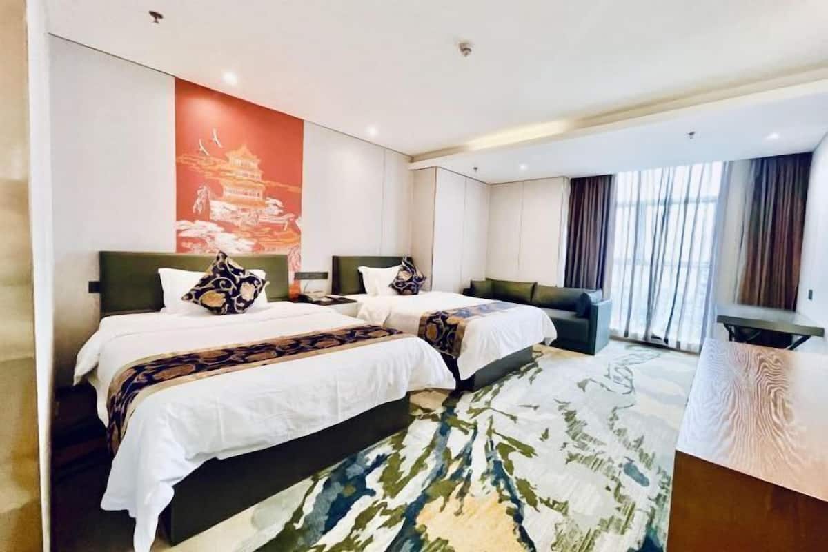 A hotel room with two beds, a sofa, a desk, and a large window with curtains.
