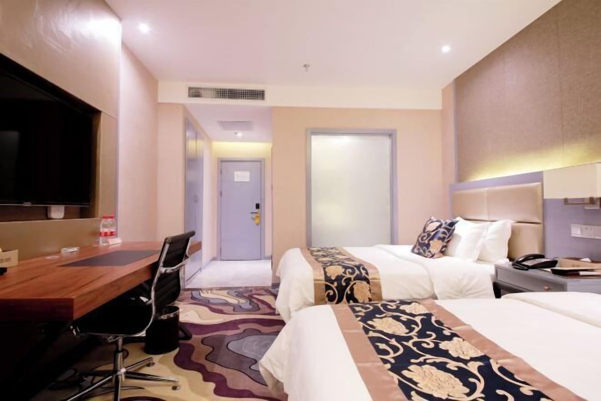 A hotel room with a bed, bedside table, chair, desk, and a television.