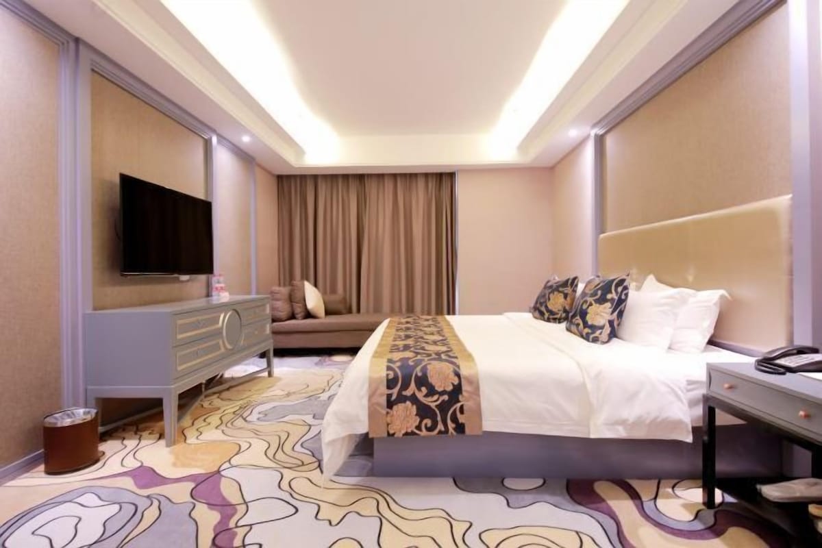 A hotel room with a bed, a TV, a sofa, and a bedside table.