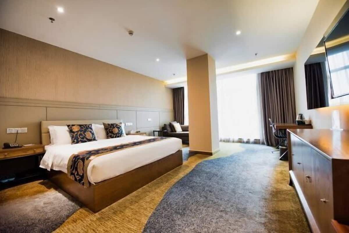 A hotel room with a large bed, a desk, a chair, a dresser, and a TV.