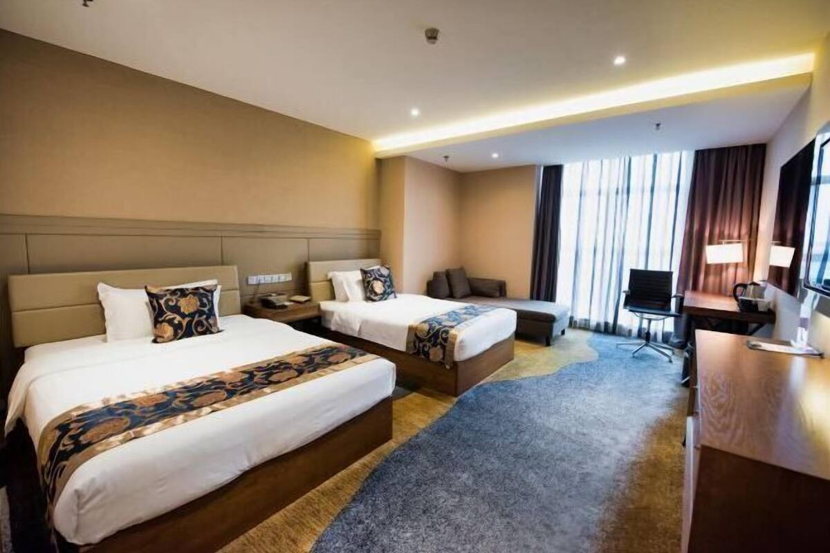 A hotel room with two beds, a desk, a chair, and a TV.