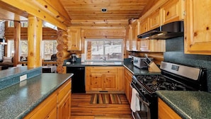 A wooden cabin interior with a kitchen area featuring a stove, microwave, and wooden cabinets.