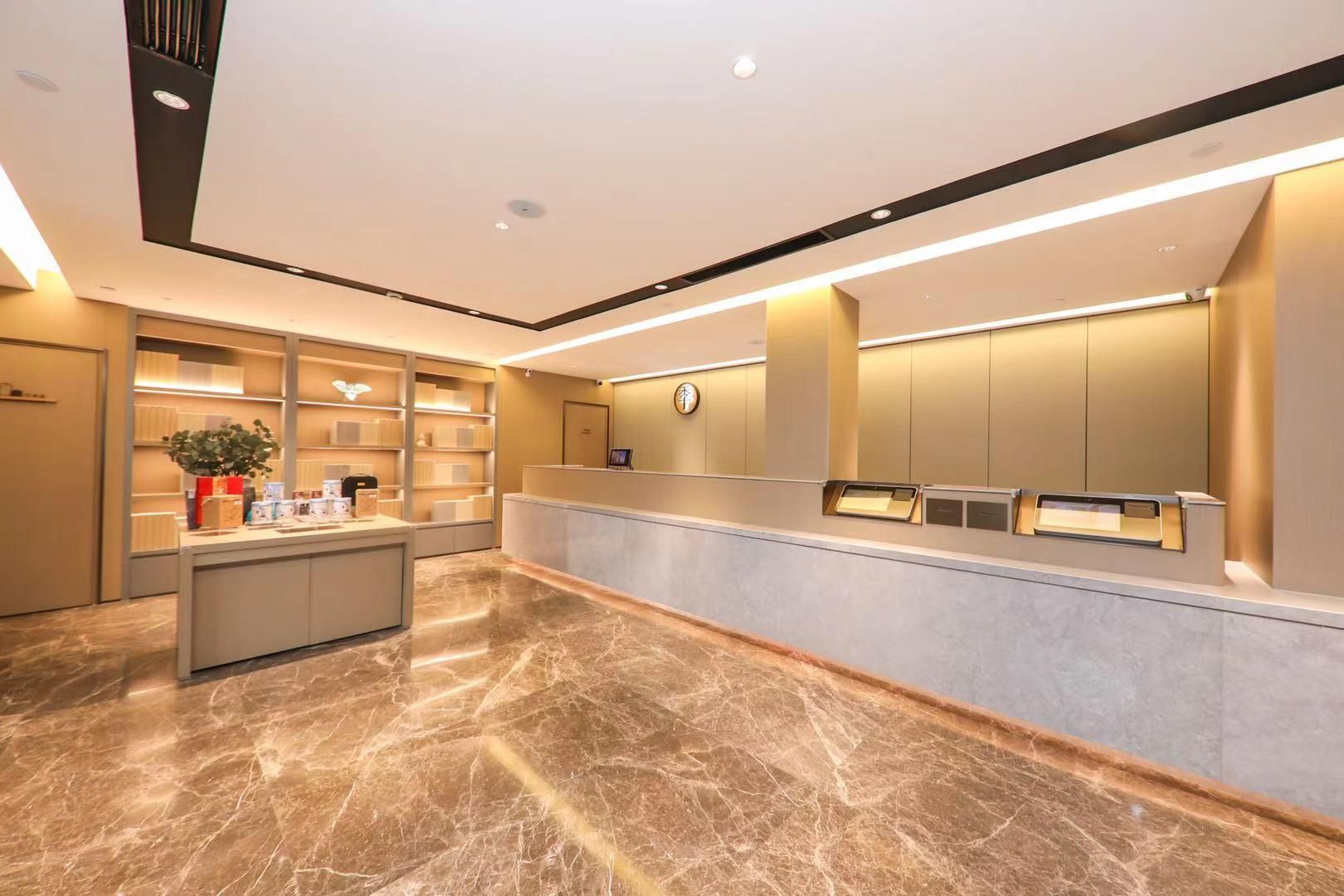 A hotel reception area with a marble floor, a reception desk, a plant, and a wall-mounted clock.