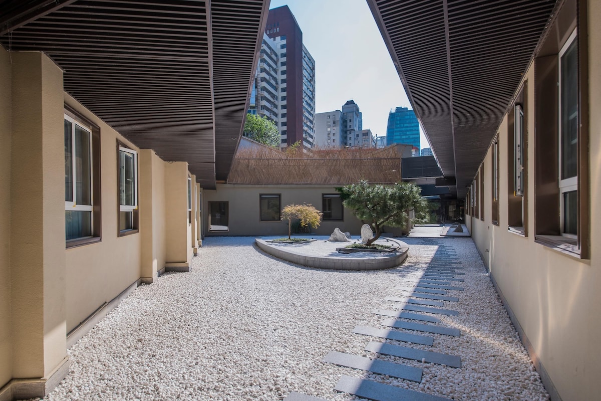 A courtyard with a gravel path, a small tree, and a building with large windows.