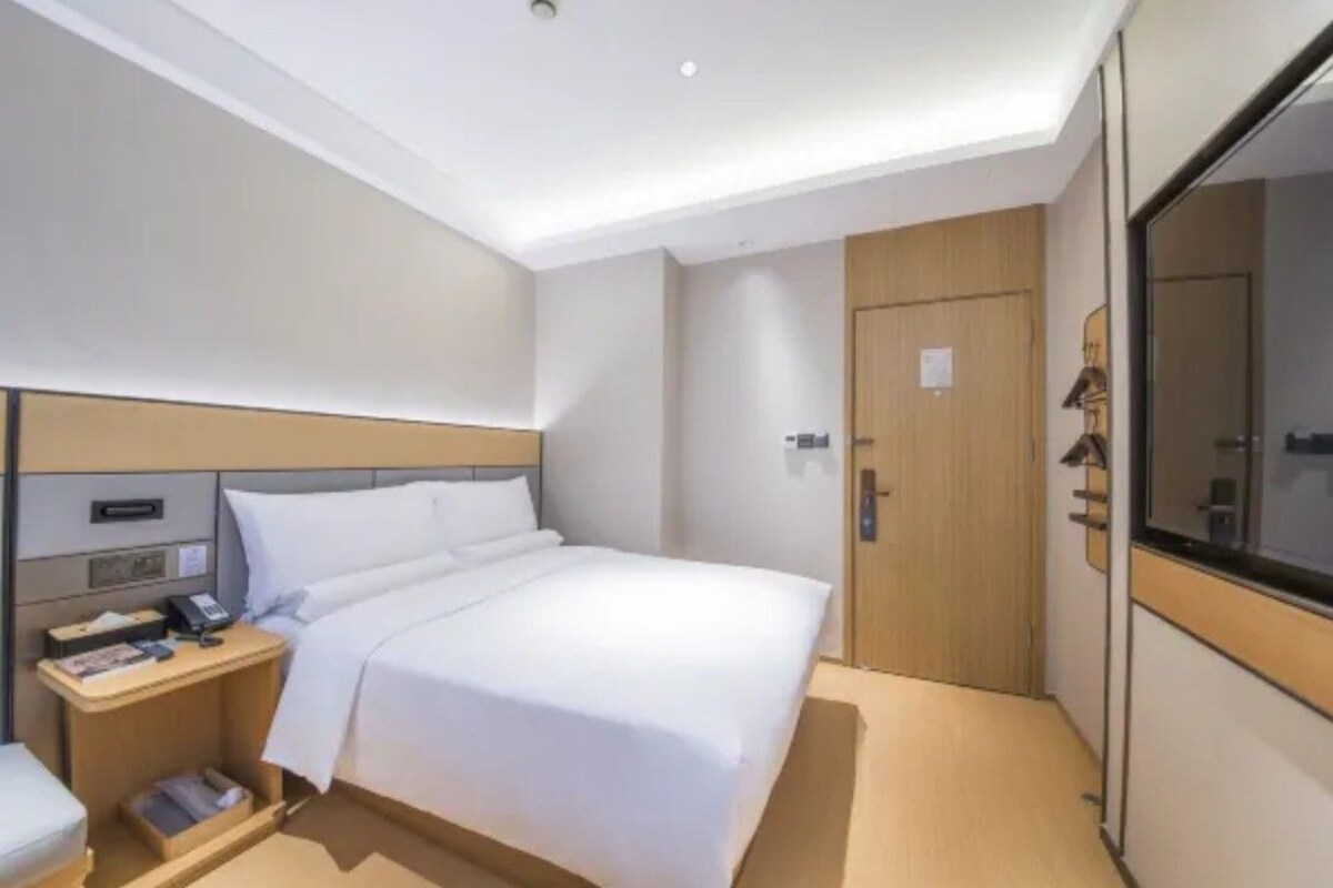 Una habitación de hotel con cama, mesita de noche, lámpara y espejo.