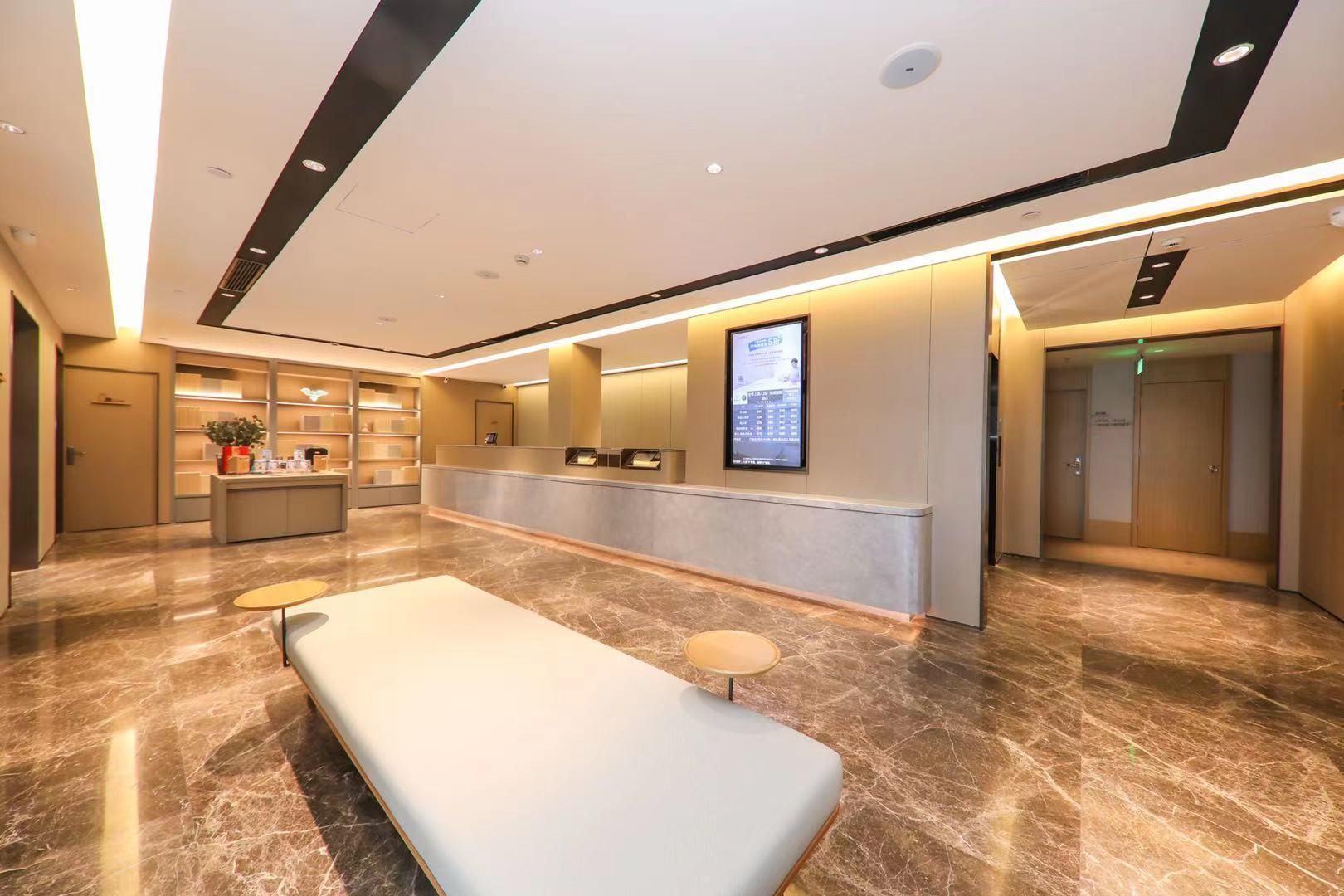 A modern hotel lobby with a reception desk, seating area, and a digital information board.