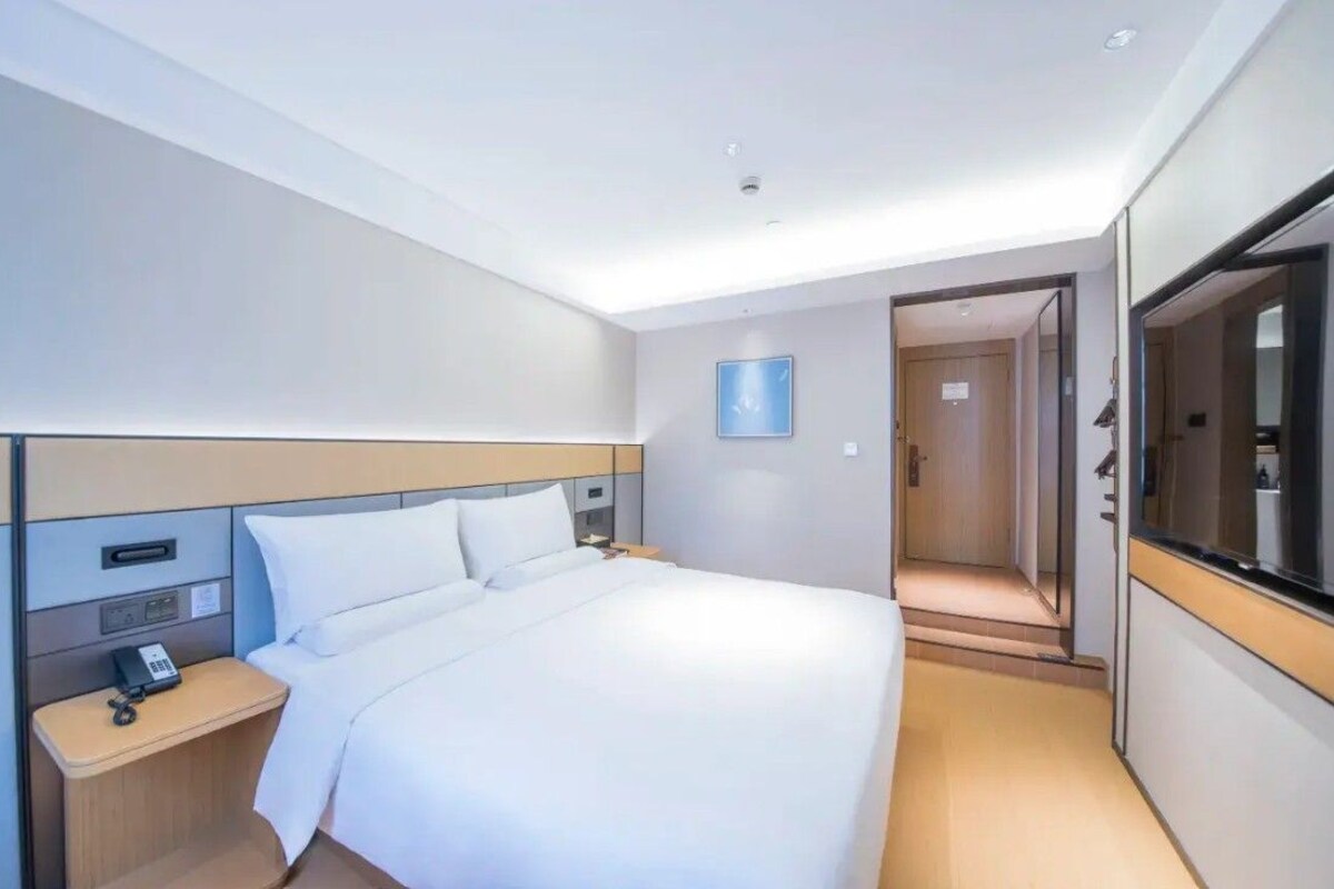 A modern hotel room with a bed, bedside table, and a large mirror.