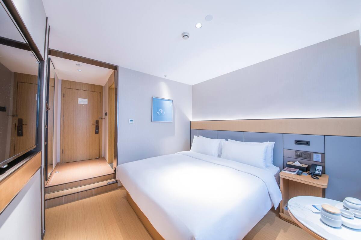 A hotel room with a bed, bedside table, and a mirror.