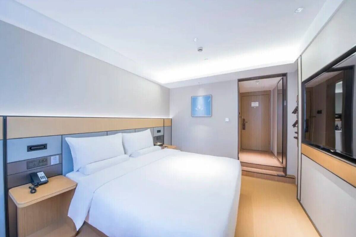 A modern hotel room with a bed, bedside table, and a large mirror.