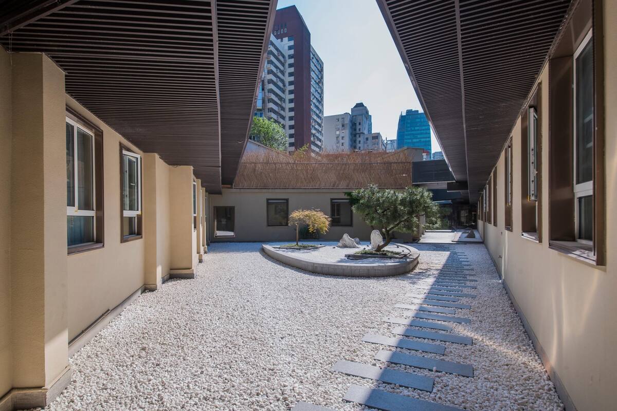 A courtyard with a gravel path, a small tree, and a building with large windows.