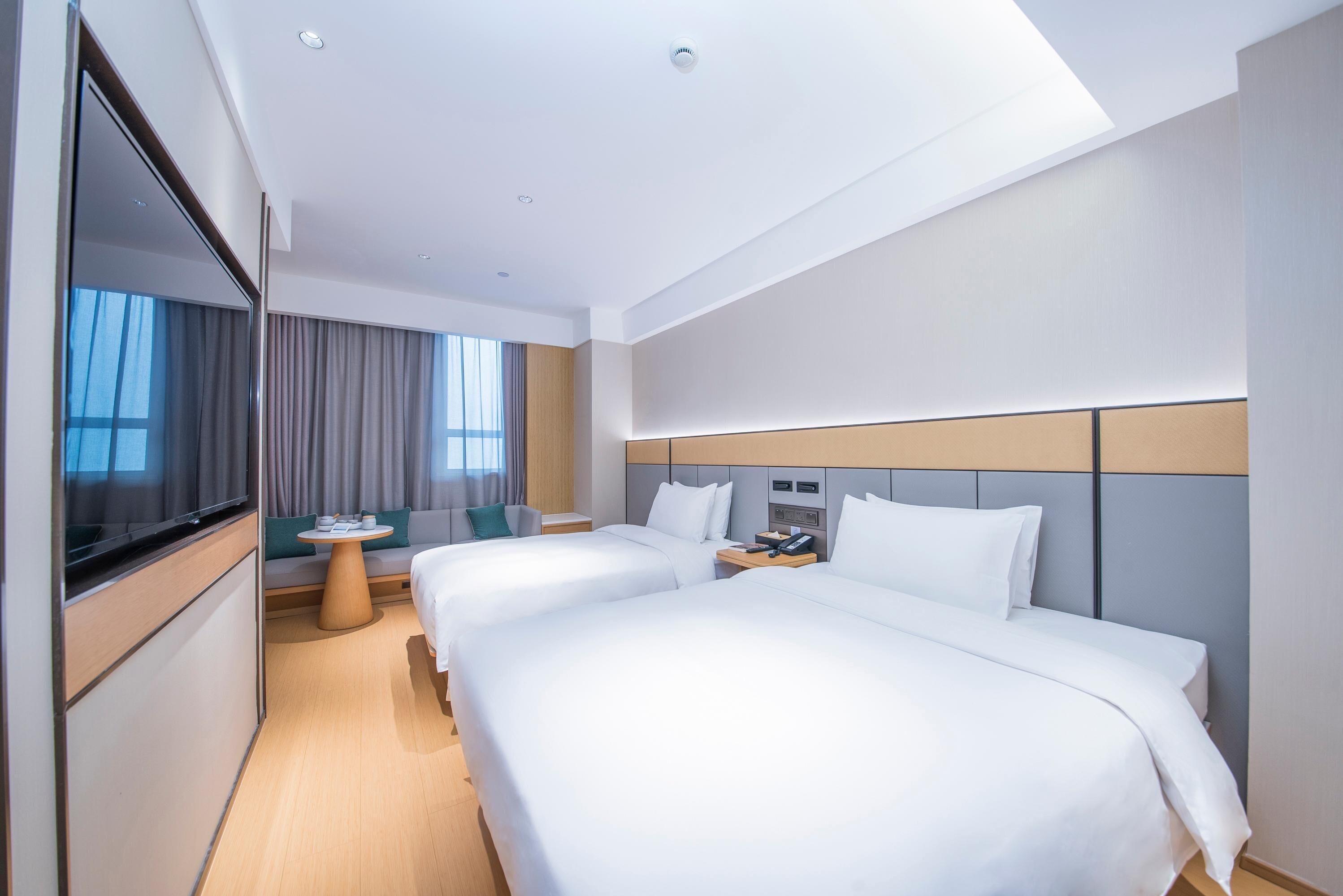 Une chambre d’hôtel moderne avec deux lits, une télévision, une petite table ronde et un canapé.