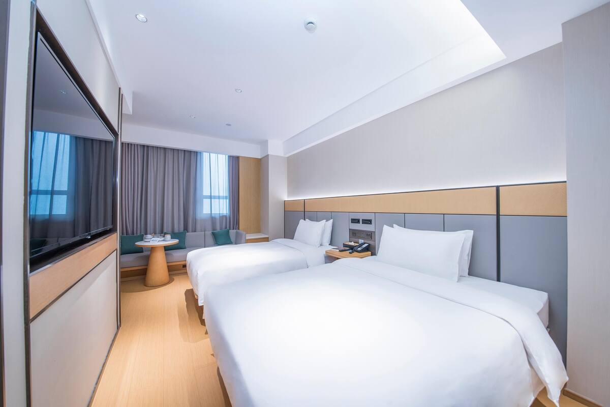 A modern hotel room with two beds, a TV, a small round table, and a sofa.
