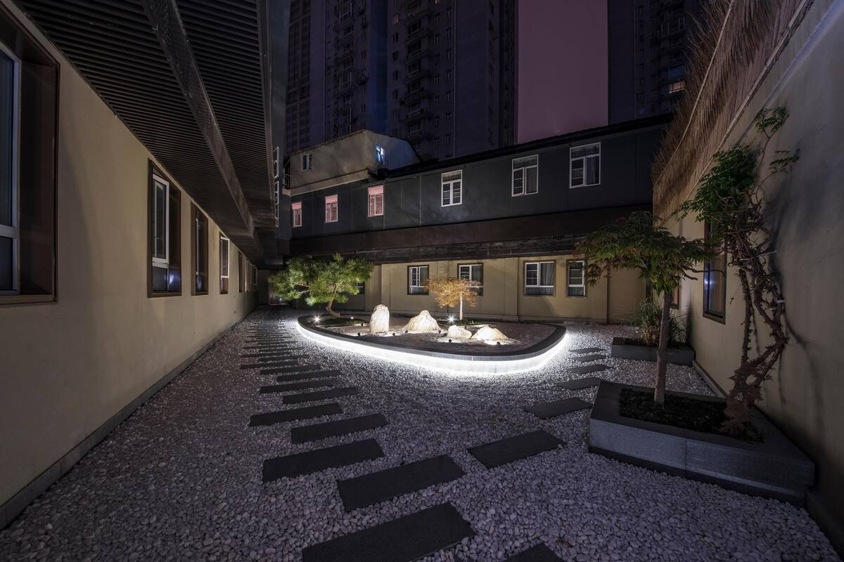 A courtyard with a pebble path, a central rock feature, and a building with multiple windows.