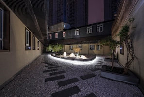 A courtyard with a pebble path, a central rock feature, and a building with multiple windows.