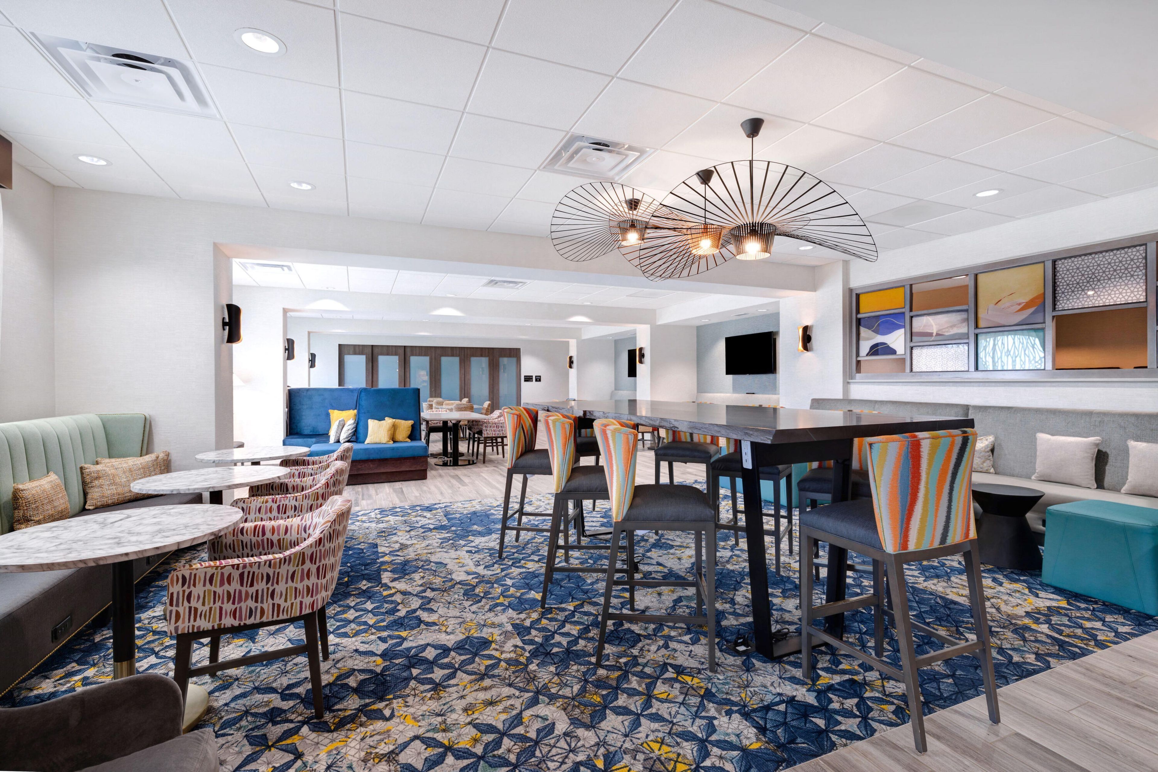 Un vestíbulo de hotel con zona de bar, disposición de asientos y alfombra estampada.
