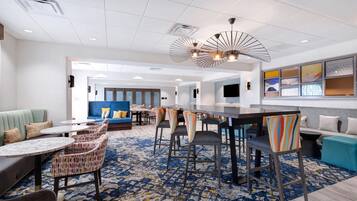 Un vestíbulo de hotel con zona de bar, disposición de asientos y alfombra estampada.