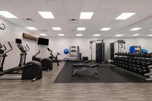 Un gimnasio con equipo de ejercicio, un televisor montado en la pared y un estante con mancuernas.