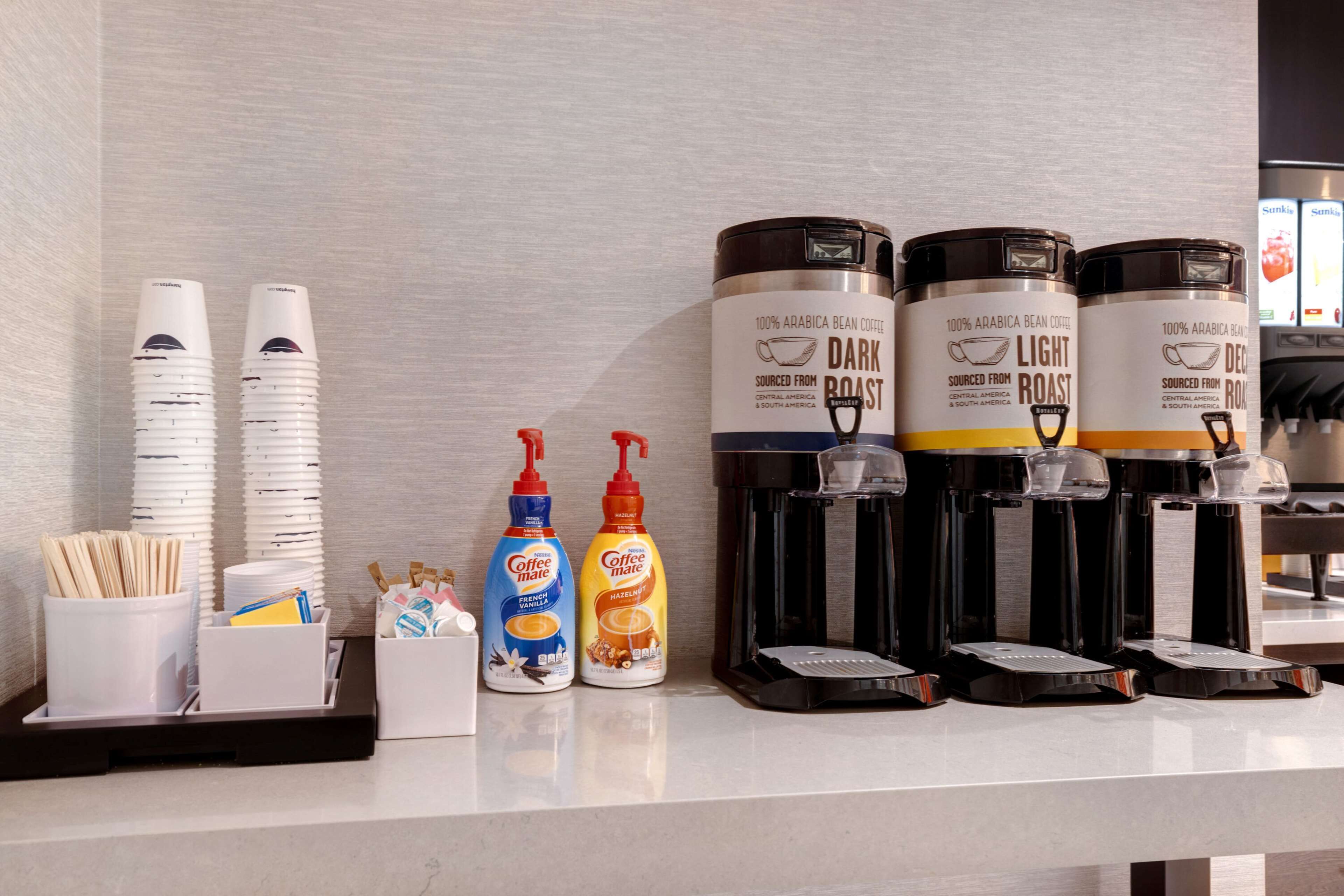 Un espace dédié au café, équipé de distributeurs de café, de gobelets jetables et de divers condiments.