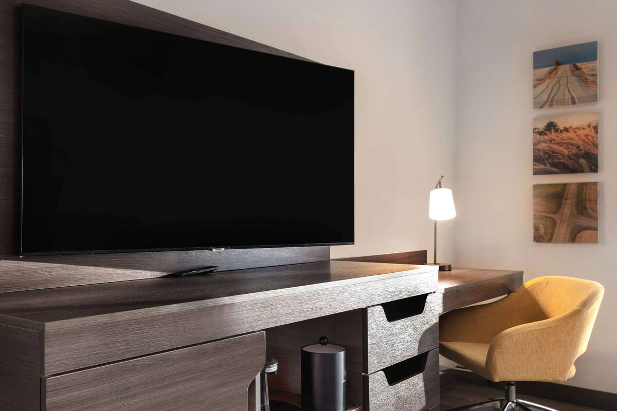 A modern room with a flat-screen TV mounted on a wooden cabinet, a yellow chair, and a lamp.