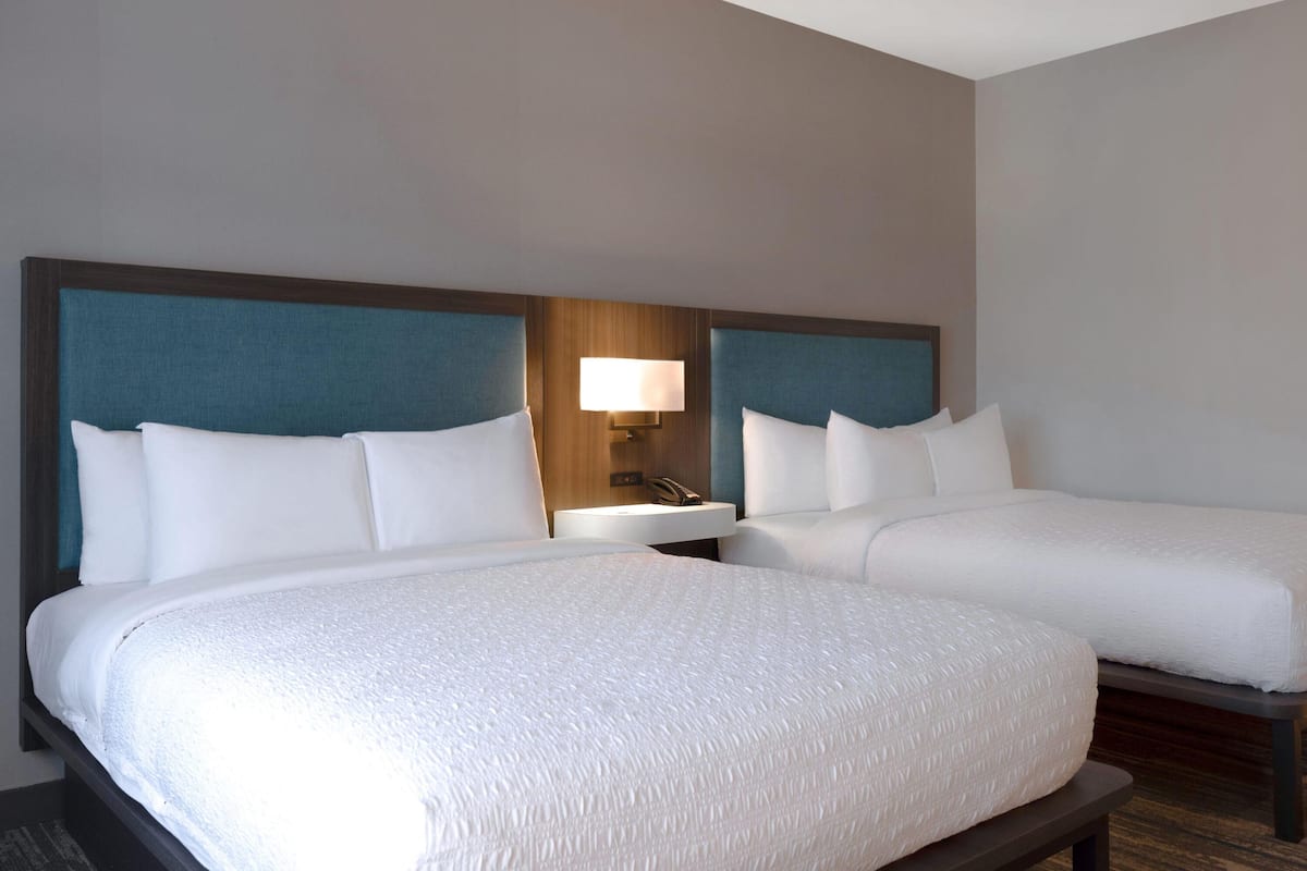 A hotel room with two beds, a nightstand, and a lamp.