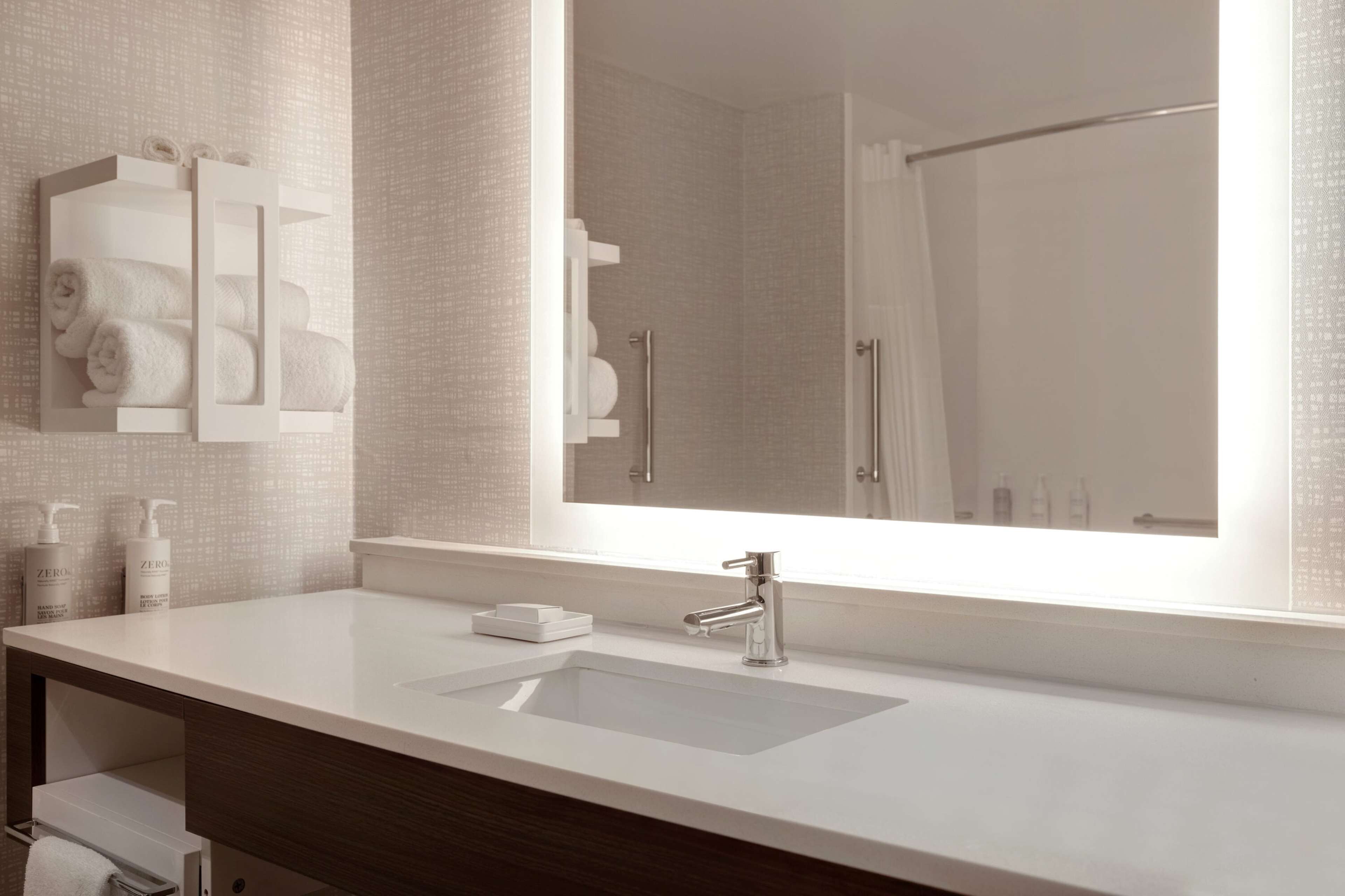 A modern bathroom with a large mirror, a white sink, and a towel rack with neatly folded towels.