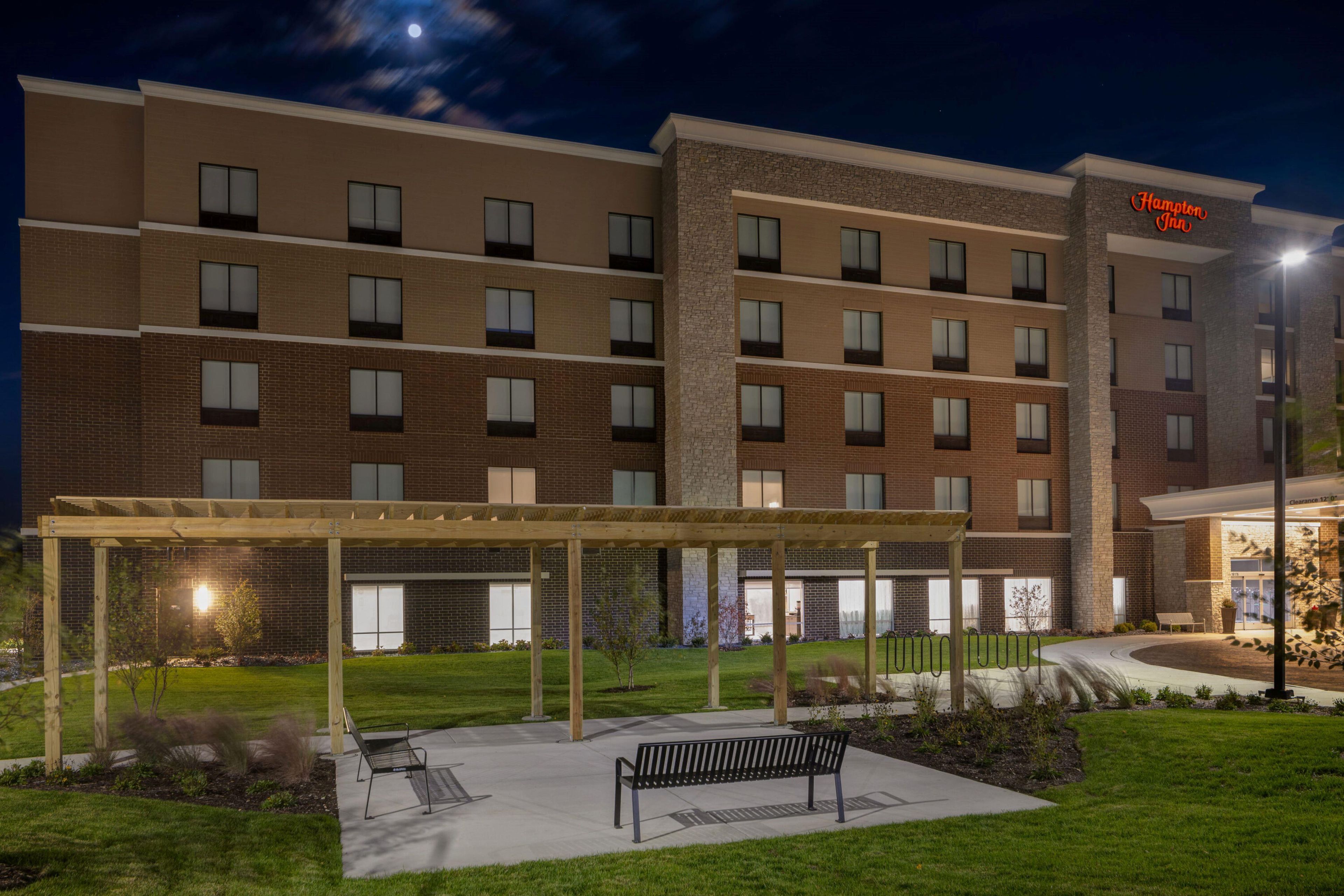 A multi-story hotel with a covered outdoor area featuring benches and a clear sky.